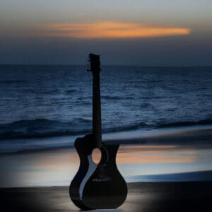 An image capturing the sleek profile of a Yamaha Silent Guitar, standing tall on a deserted beach at sunset